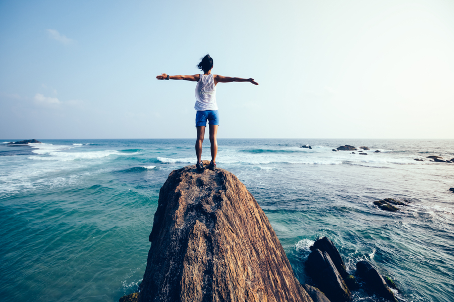 Freedom young woman outstretched arms on seaside rock cliff edge